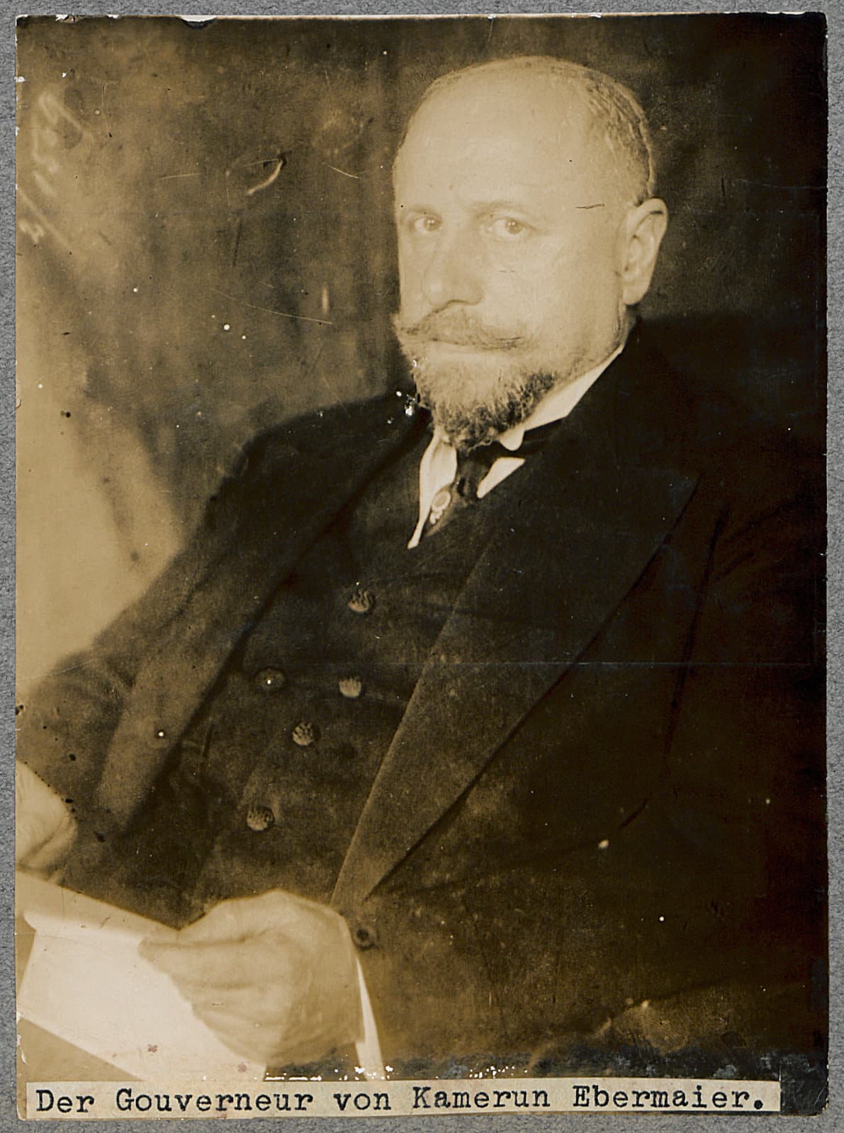Portrait photographique de Karl Ebermaier, homme chauve à barbe courte, en costume sombre, tenant un document, légendé « Der Gouverneur von Kamerun Ebermaier ».