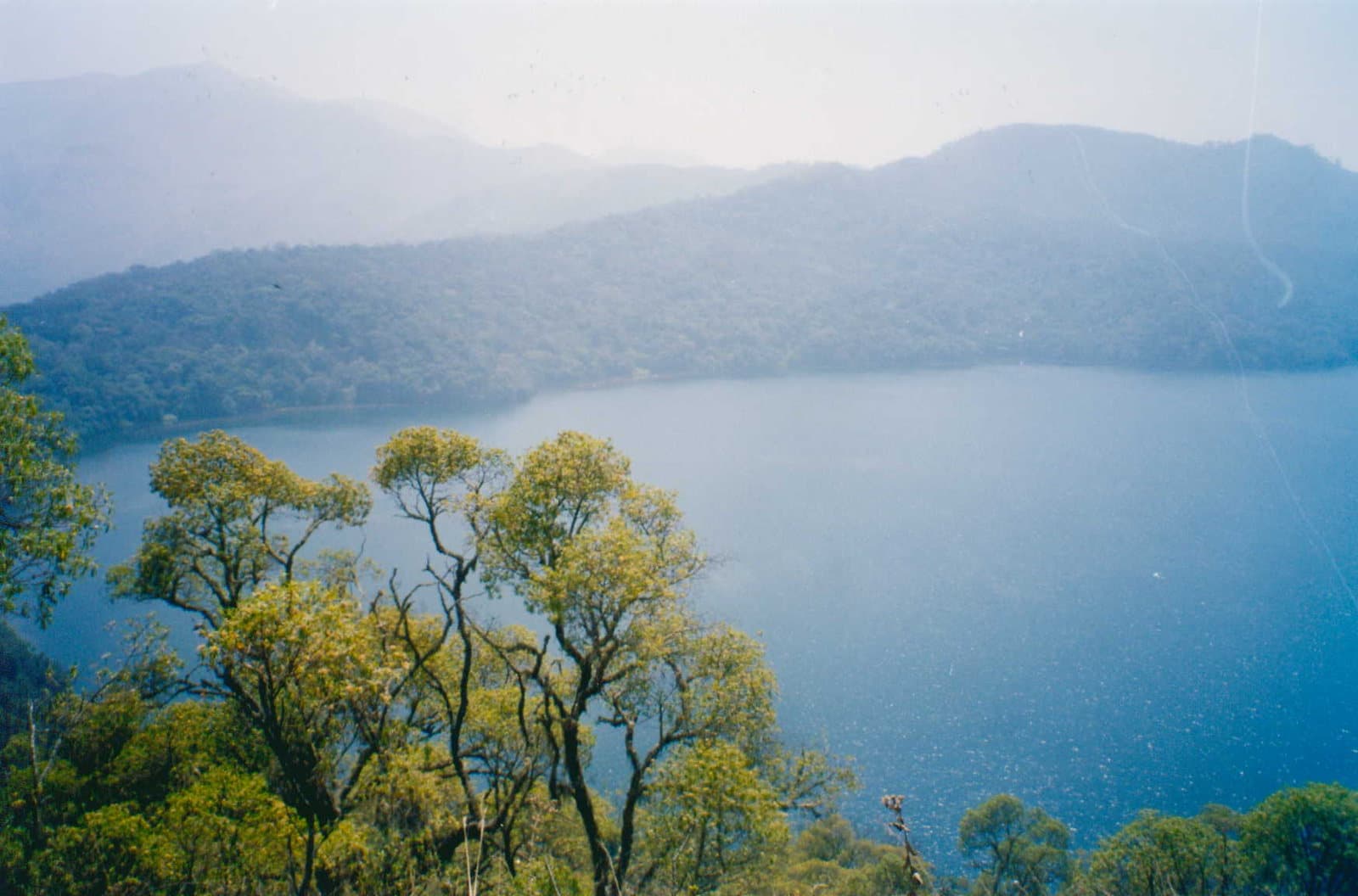 Surface calme du lac Oku entourée de collines boisées, Cameroun.