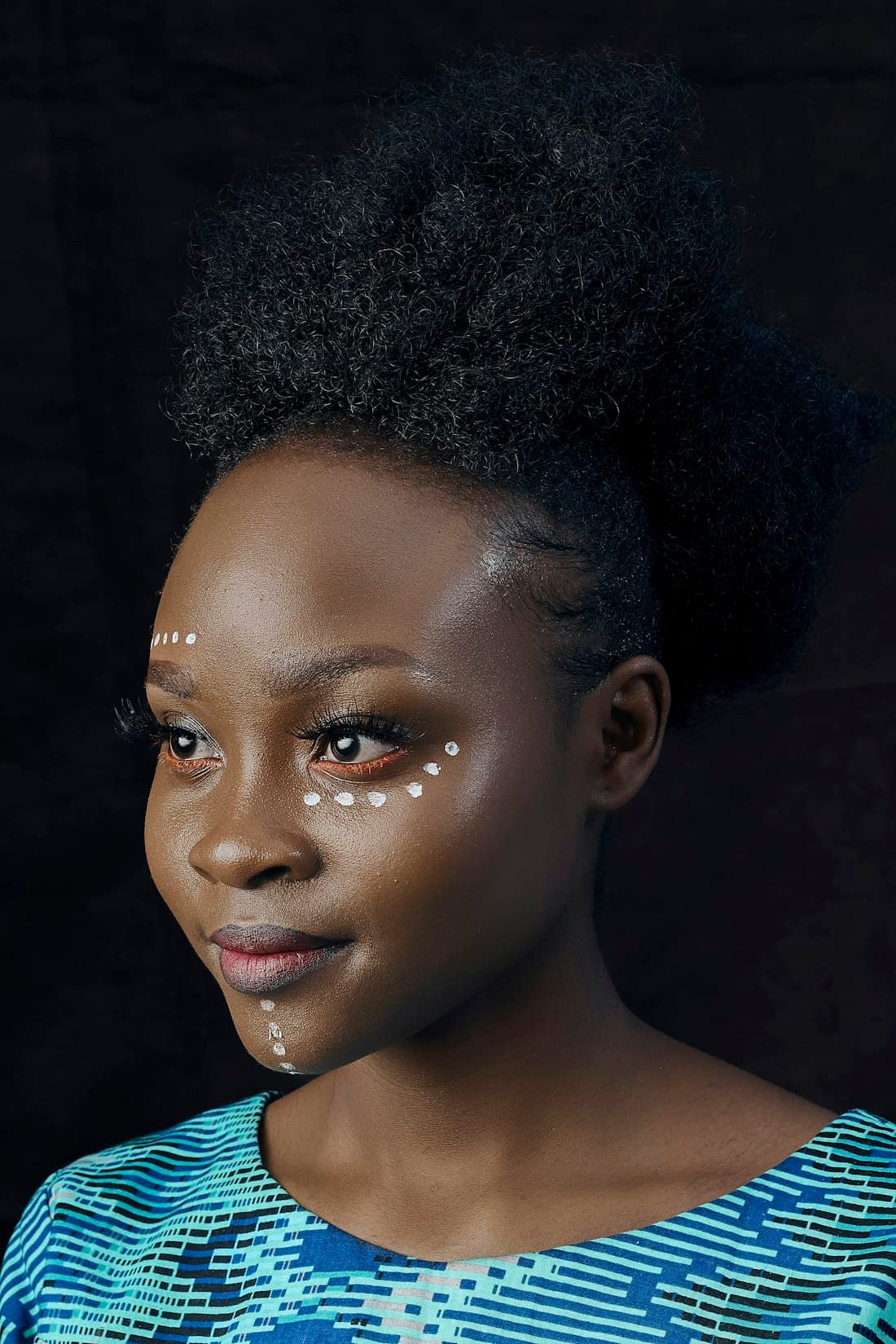 Portrait d'une jeune femme au regard confiant, motifs traditionnels peints sur le visage.