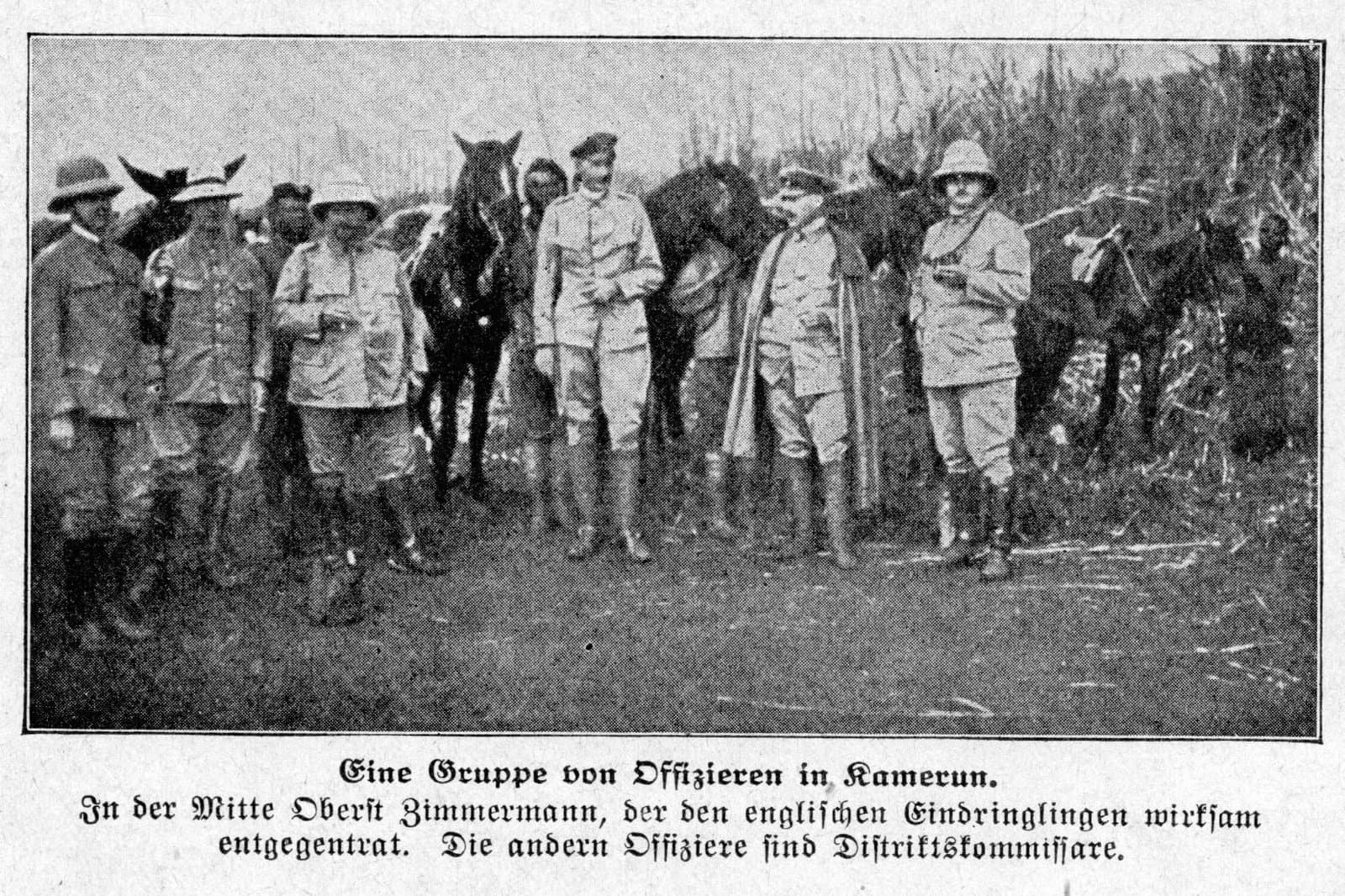 Groupe de sept officiers coloniaux allemands en tenue claire et casques coloniaux, debout avec des chevaux en lisière de forêt ; légende allemande identifiant le colonel Zimmermann au centre.