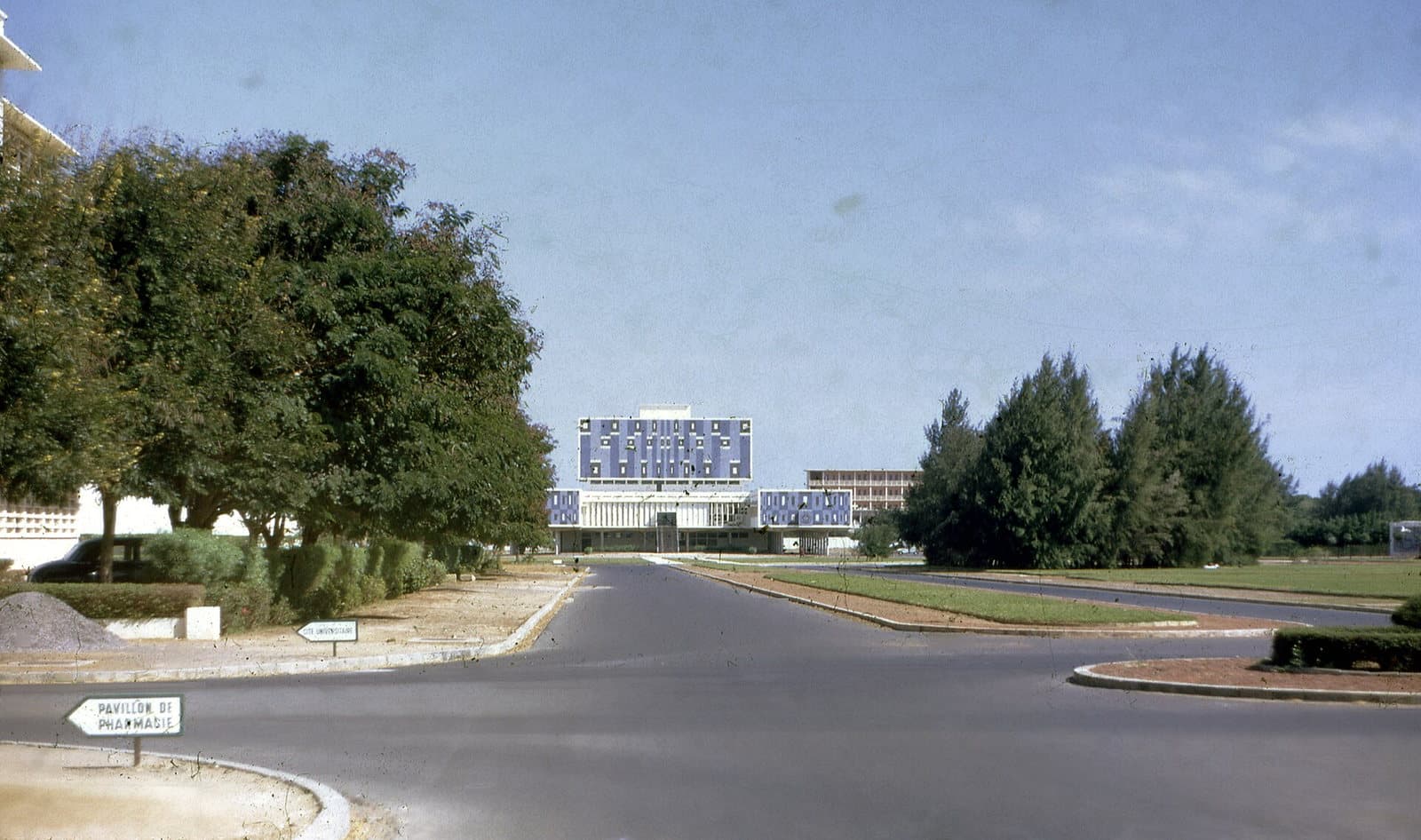 Vue d'une allée du campus universitaire de Dakar en 1967, avec un bâtiment moderne des années 1960 au fond.