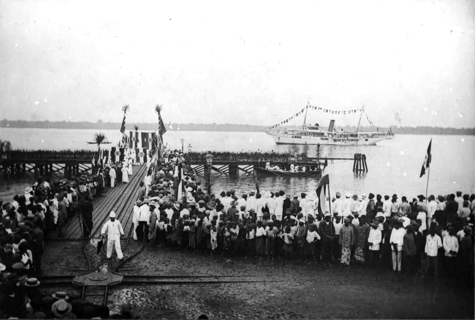 Photographie ancienne en noir et blanc d'un ponton en bois avançant sur l'eau à Douala, avec un navire à l'arrière-plan, entre 1902 et 1908.