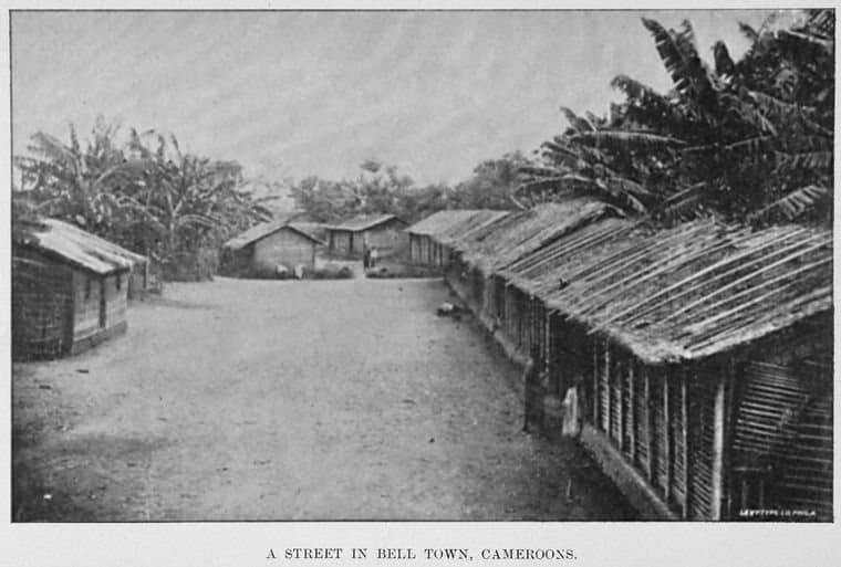 Photographie ancienne en noir et blanc d'une rue bordée d'habitations en bois à Bell Town, quartier duala de Douala, en 1895.