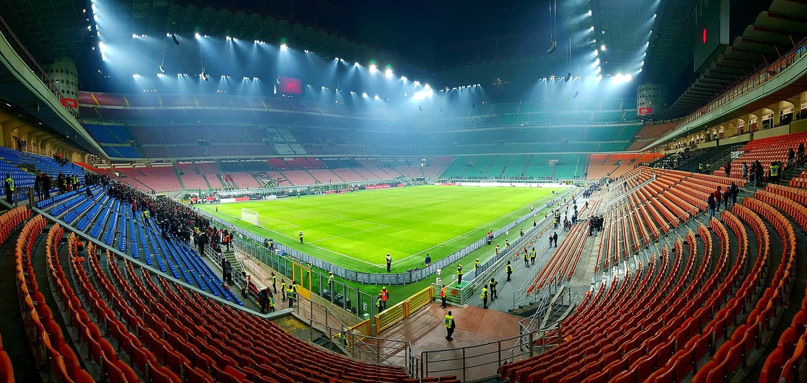 Vue intérieure du stade San Siro à Milan de nuit, gradins et pelouse éclairés par les projecteurs.