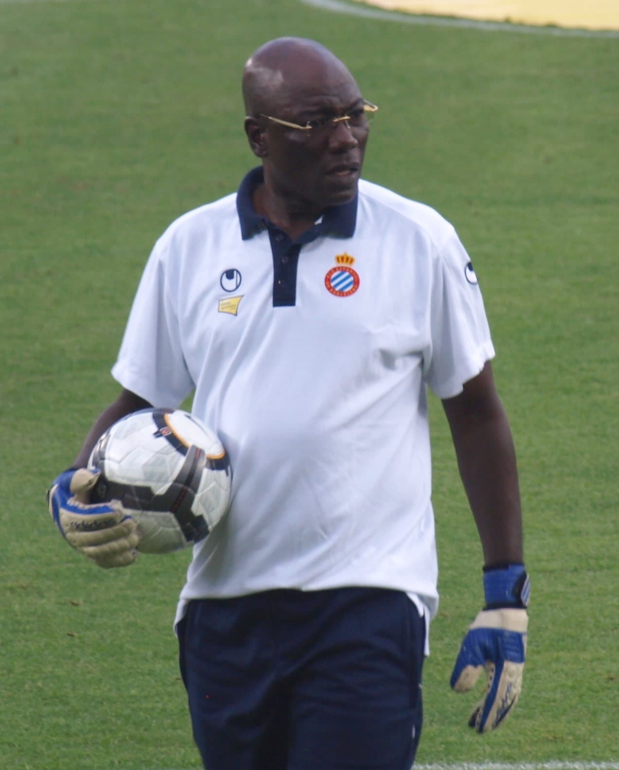 Thomas N'Kono, ancien gardien camerounais, en tenue d'entraîneur sur un terrain, un ballon sous le bras.