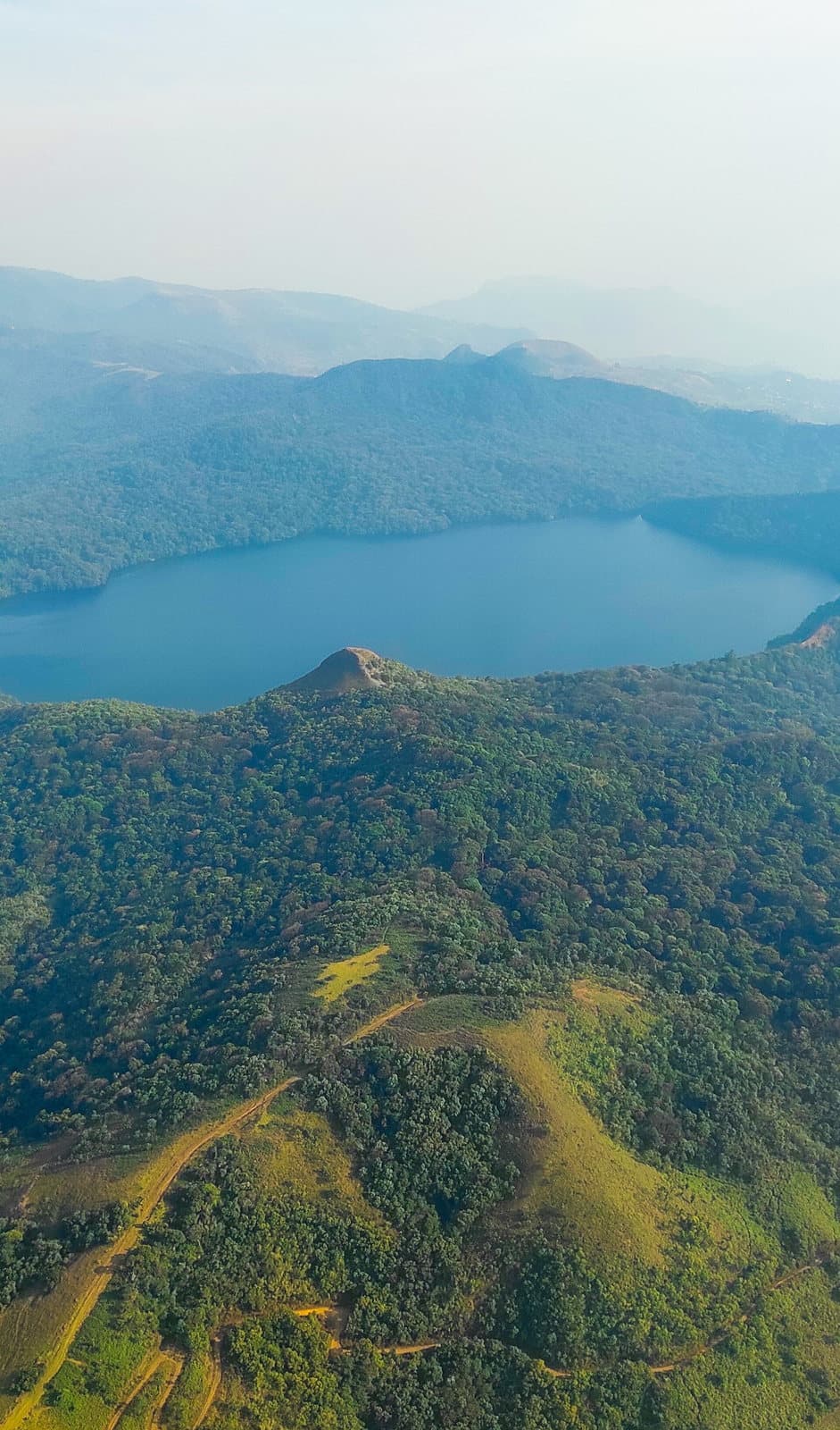 Lac bleu niché au creux d'un massif entièrement recouvert d'une forêt de montagne dense, vu du ciel.