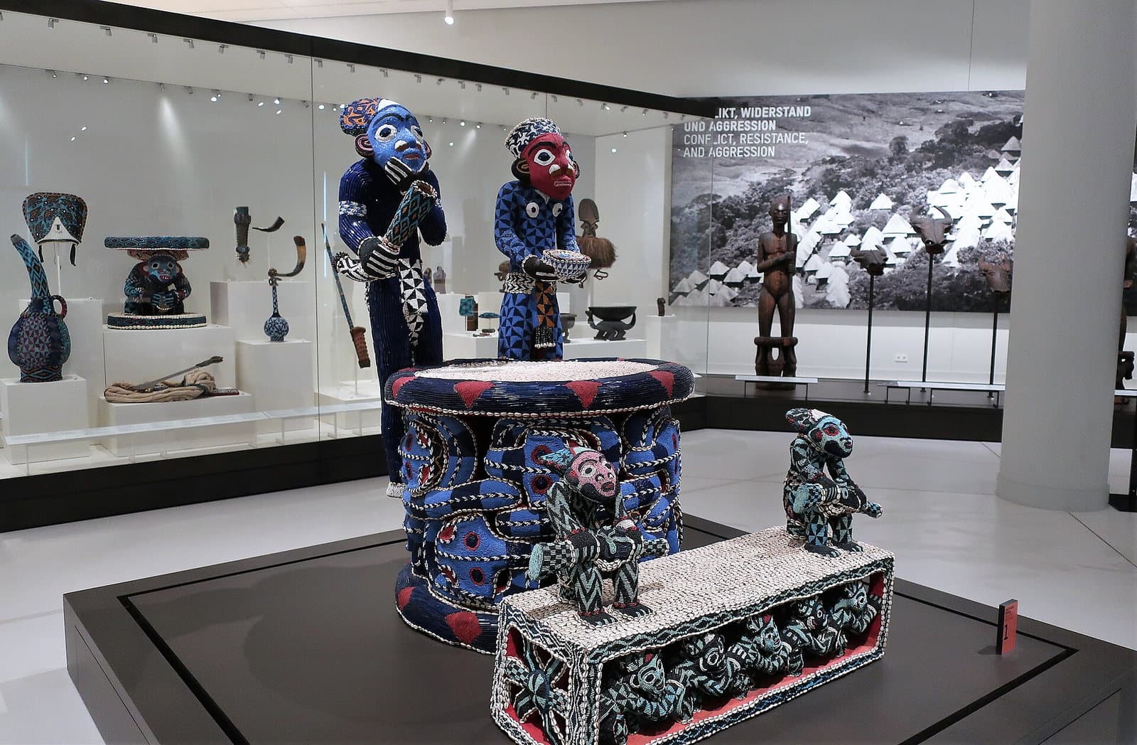 Trône royal bamoum entièrement recouvert de perles bleues, blanches et rouges avec deux figures humaines perlées, dans une vitrine de musée à Berlin.