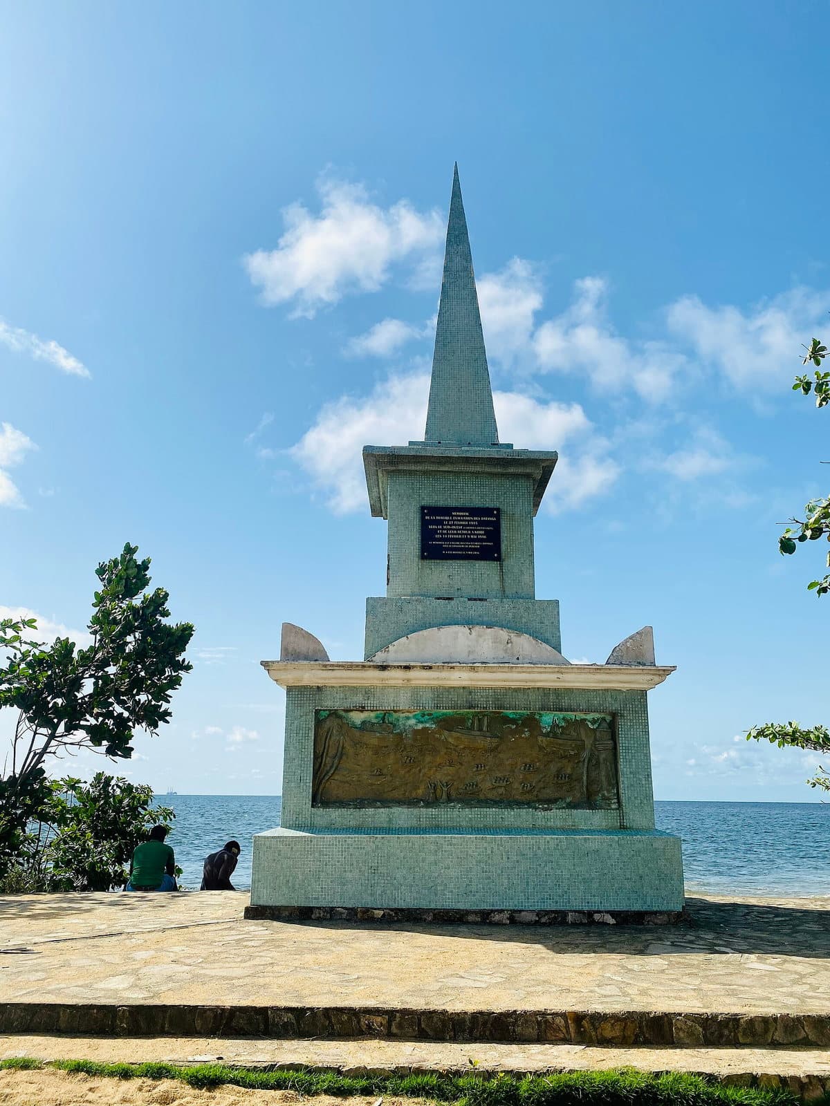 Monument en béton peint en vert, structure carrée surmontée d'une pyramide, le Mémorial de la Tragédie de Batanga à Kribi.