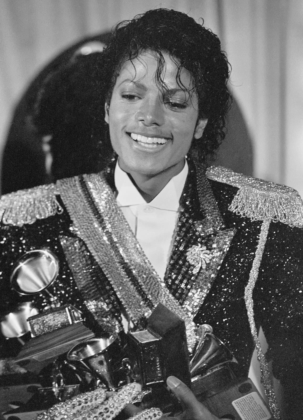 Photographie de presse en noir et blanc de 1984 montrant Michael Jackson tenant plusieurs trophées Grammy Awards.
